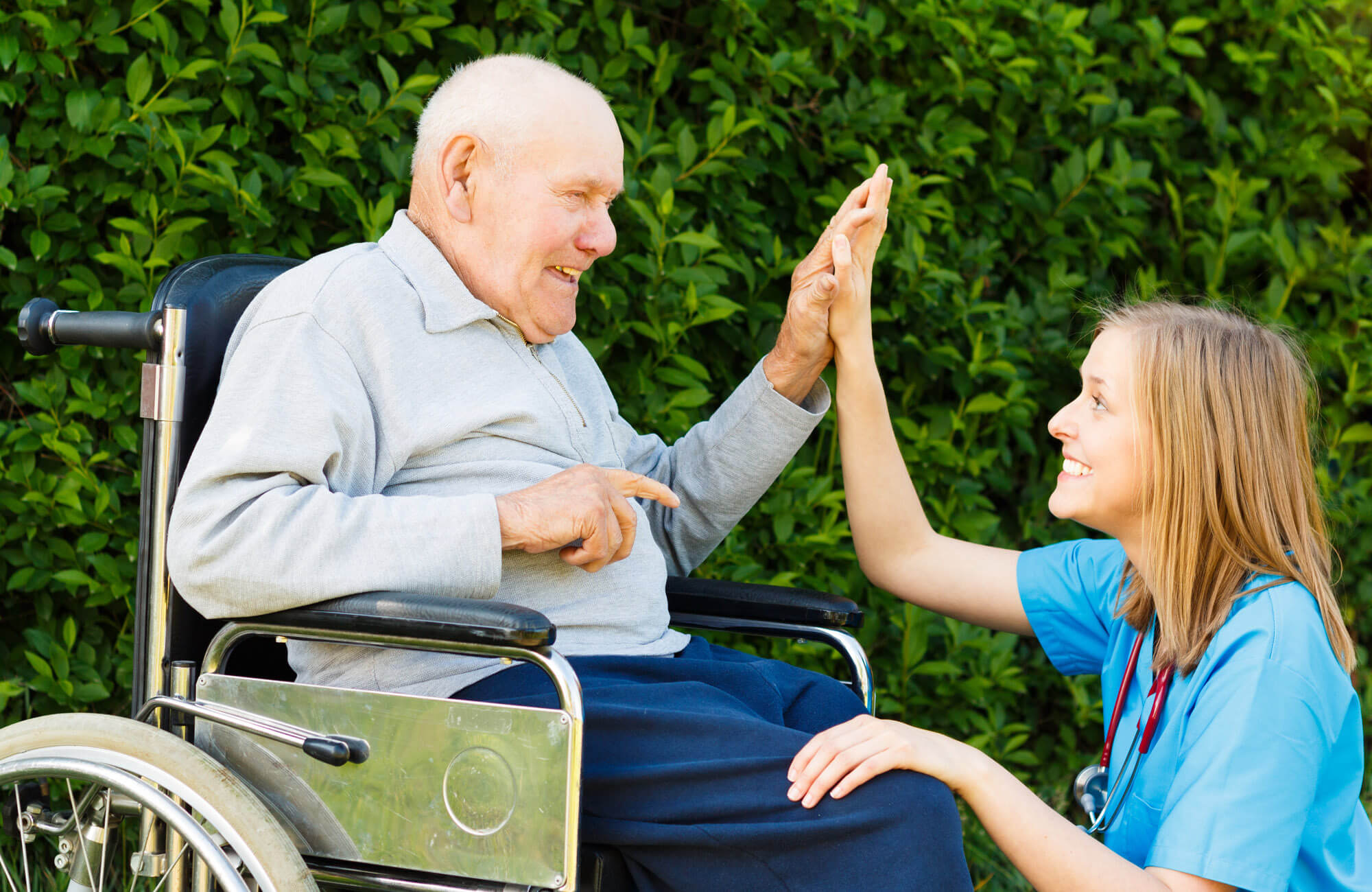 Young woman giving a high-five to an elderly man in a wheelchair.