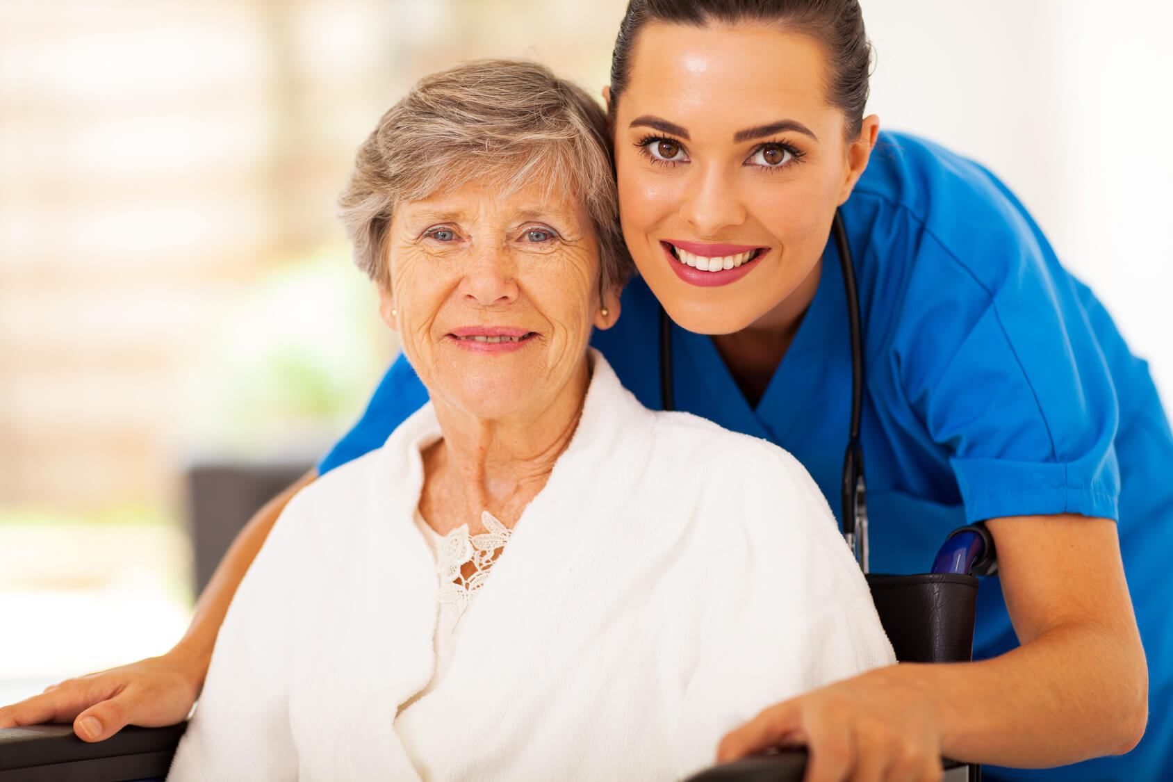 A nurse smiling with an elderly woman in a wheelchair.